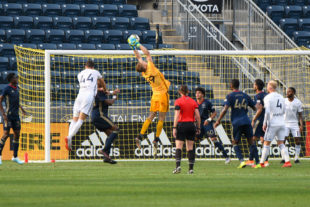 Morton makes a great save, jumping to get his hands on the ball. His teammates look on ready to assist him if needed.