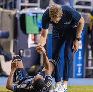 Philadelphia Union Head Coach Jim Curtin extends a hand to help José Martínez up from the ground.