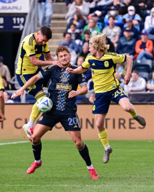 Bruno Damiani fights to get to the ball after a header as Gastón Brugman has his hands pressing on his neck and shoulder.