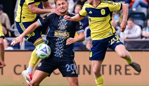 Bruno Damiani fights to get to the ball after a header as Gastón Brugman has his hands pressing on his neck and shoulder.